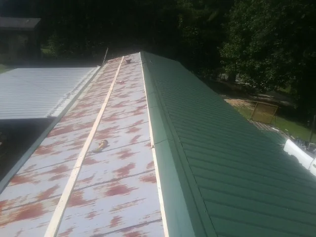 Old rusted panels beside newly installed green metal roofing — Wind Damage Roof Repair by Roofing Brothers in Roosevelt
