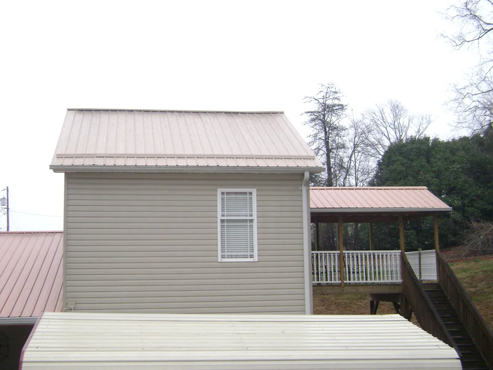 Tan metal roofs on a two story addition and attached porch, from a Roof Replacement job in Roosevelt